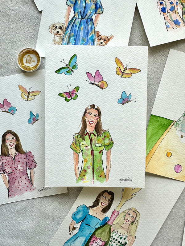 a flat lay of watercolor portrait illustrations of women with background of butterflies, champagne and small dogs